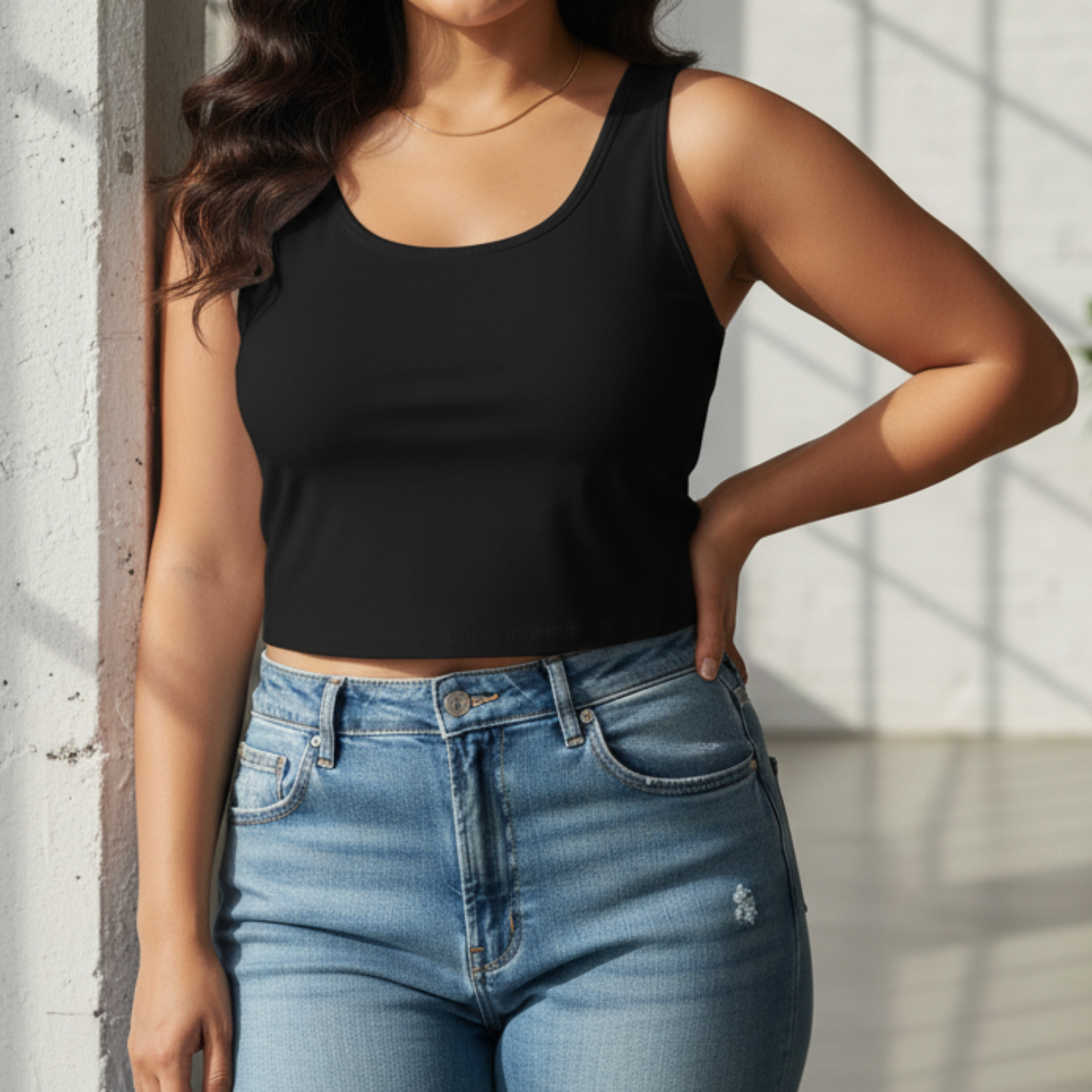 Person wearing a black tank top and blue jeans against a light background