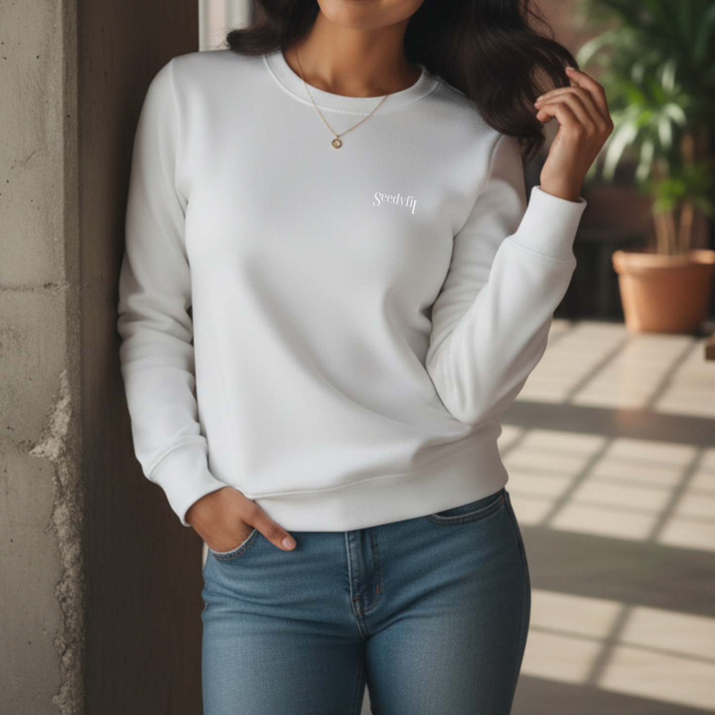 Person wearing a white sweatshirt with text, standing indoors with plants in the background.