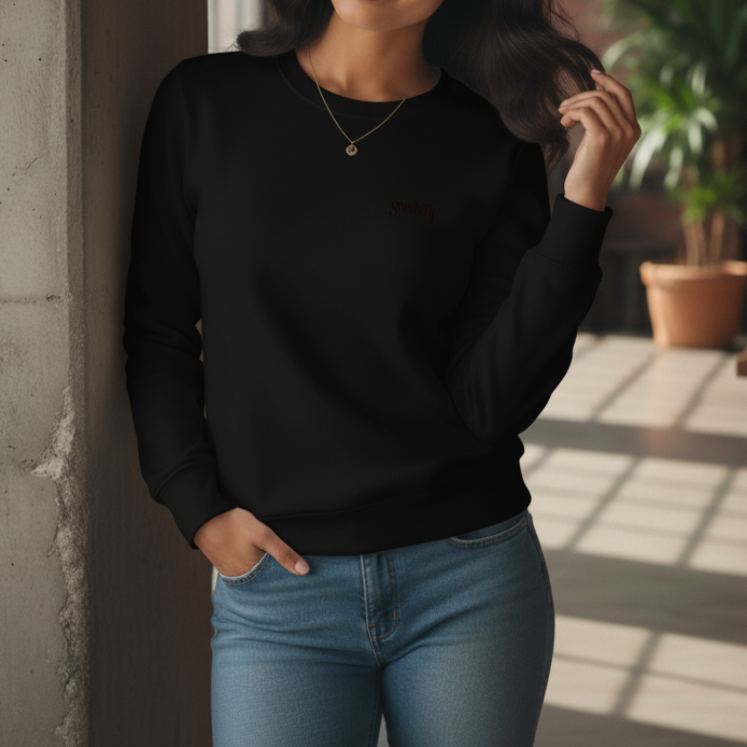 Person wearing a black sweatshirt and blue jeans standing against a wall with sunlight casting shadows.